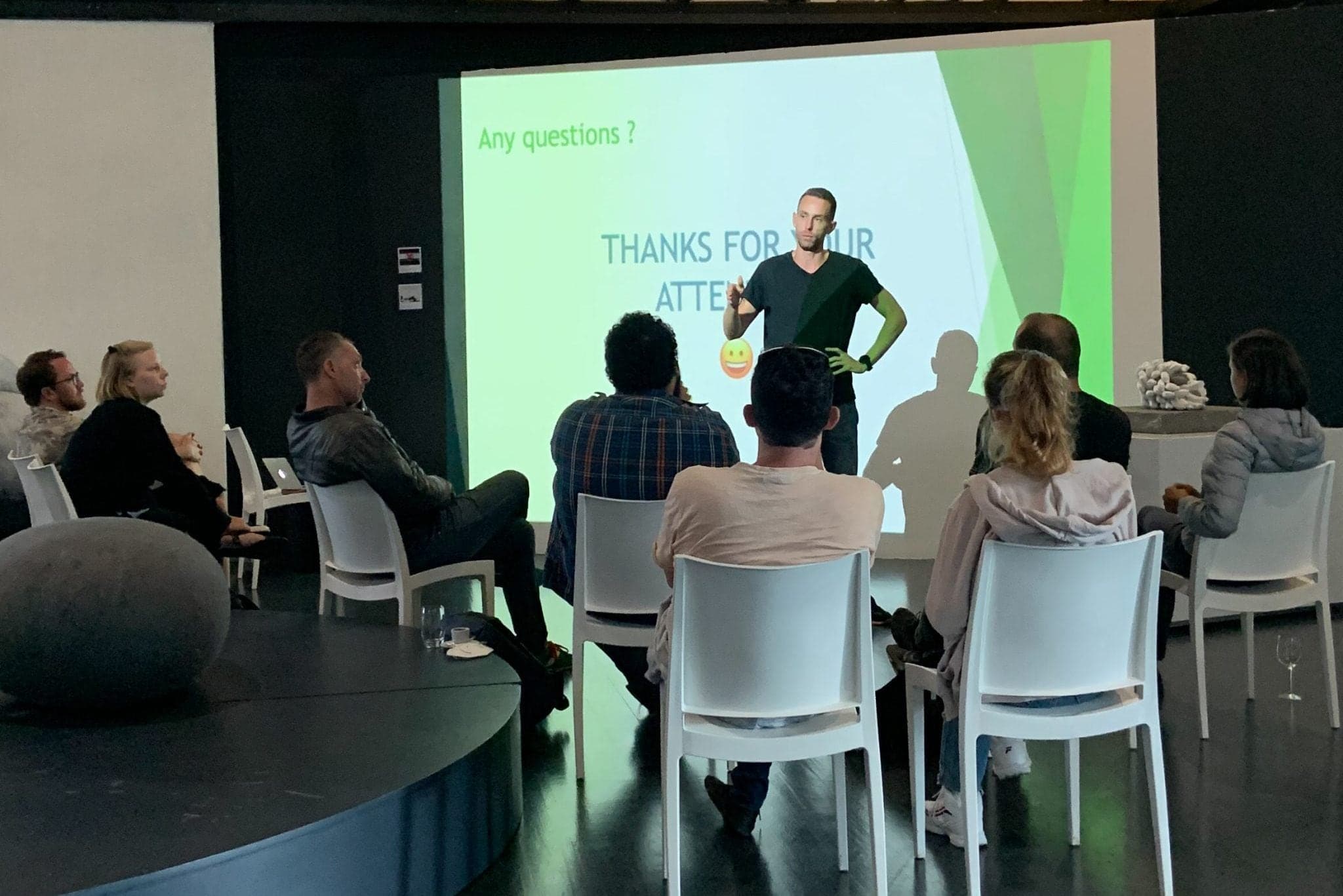 Adrien Hardy standing before a projected slide, answering questions from a seated audience