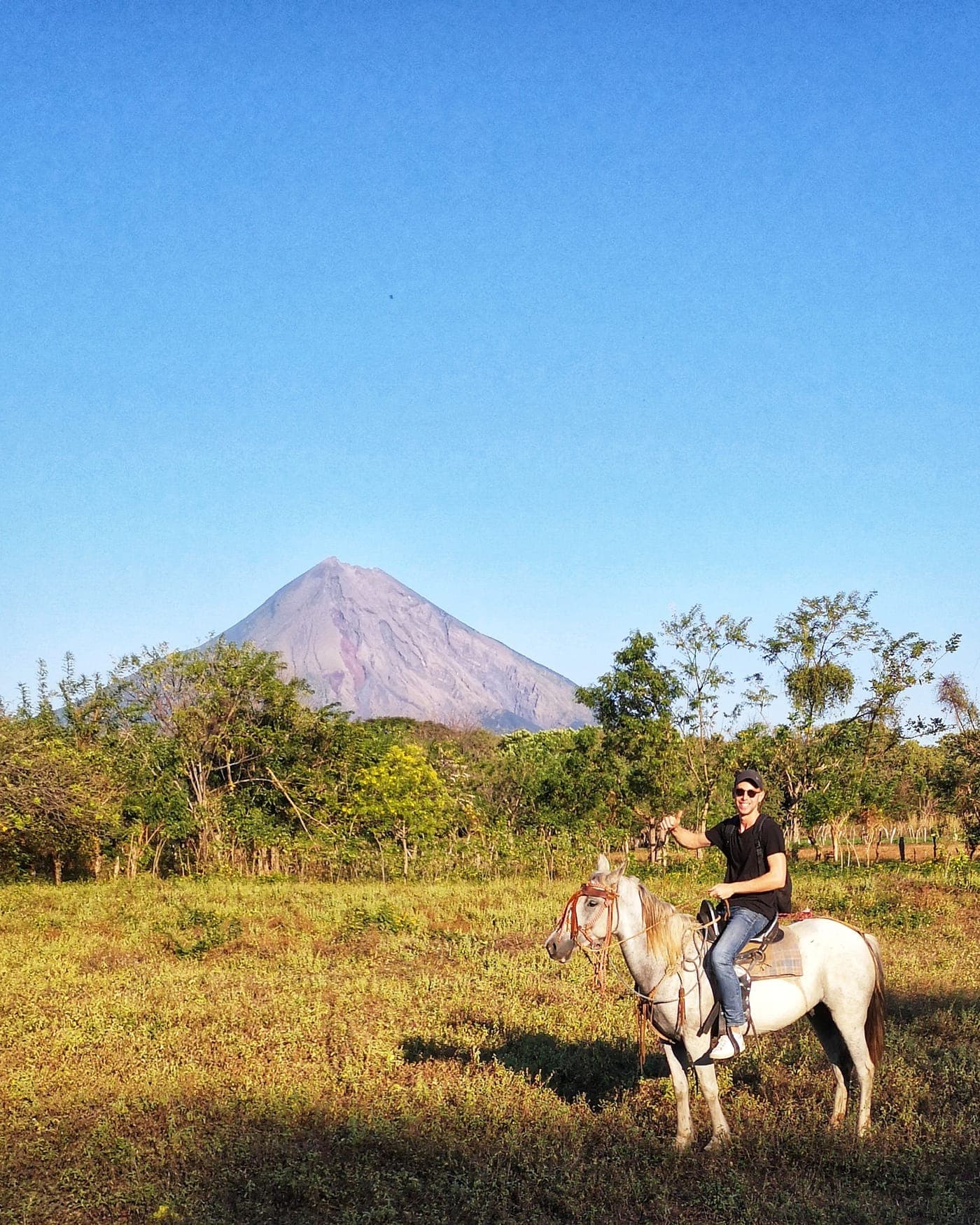 A rider on horseback crossing a green field below a volcano