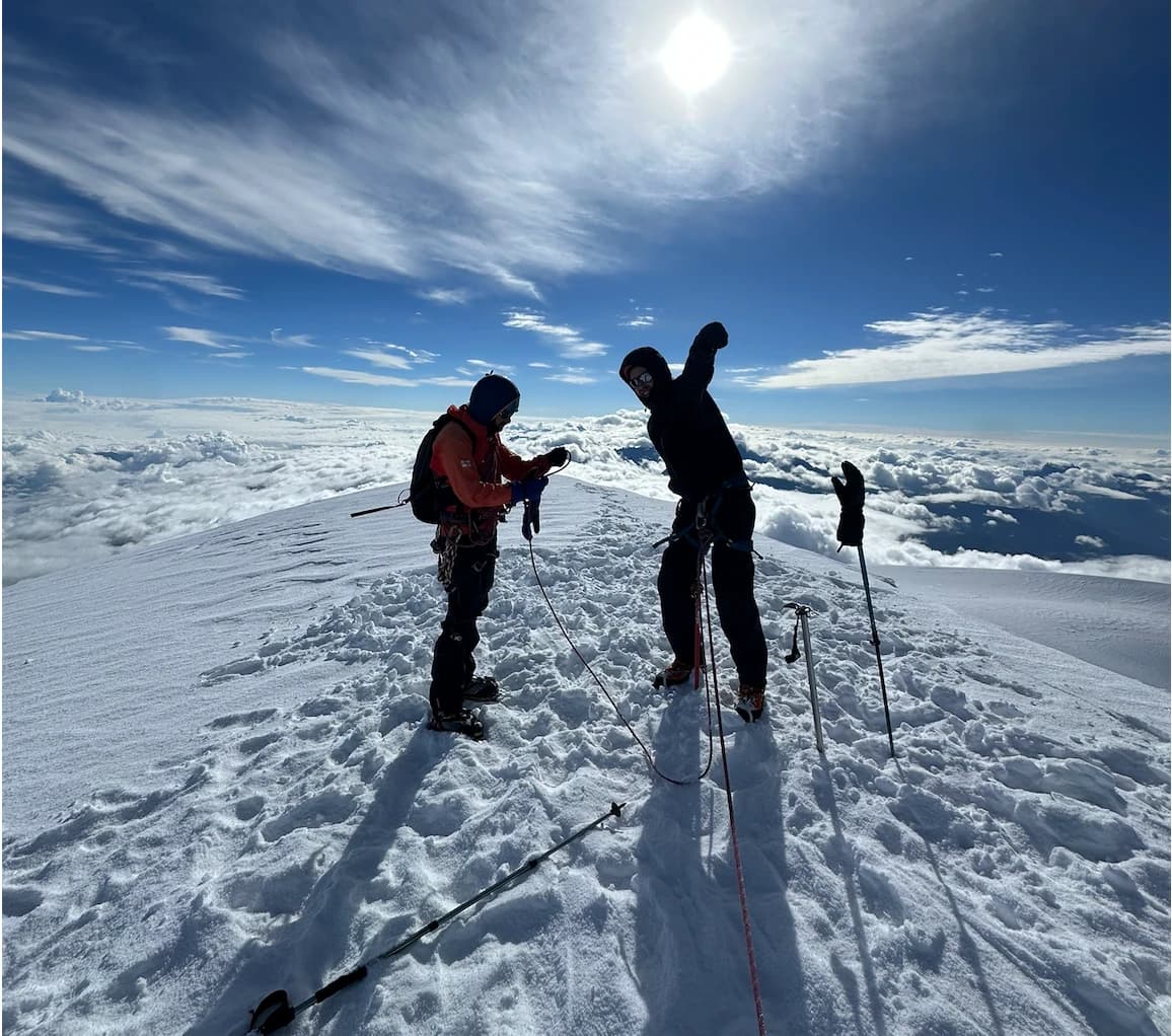 Two climbers roped together on the summit ridge of Mount Kazbek, above a sea of clouds